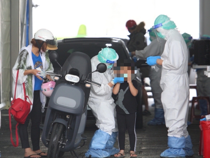 本土疫情升溫，一位家長帶著小孩騎車前往排隊篩檢。（張鎧乙攝）