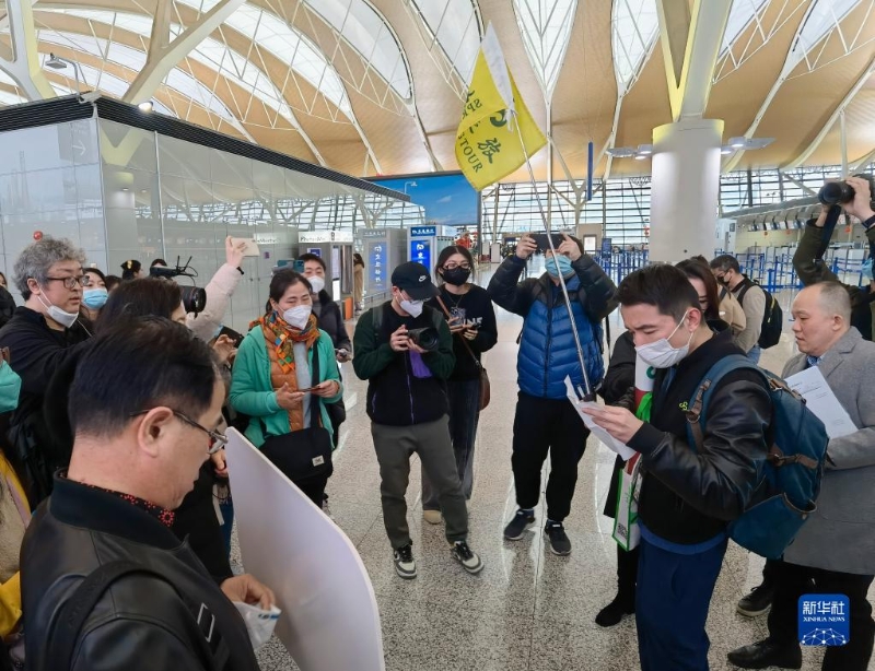 2月6日，在上海浦東國際機場，出境團隊游領(lǐng)隊師文（舉旗者）向游客說明相關(guān)注意事項。（圖源：新華社）